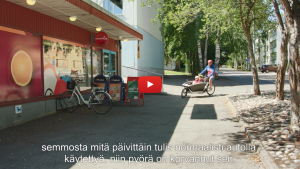 Linkki Virtaa fillariin -kokeilun 2018 minidokumenttiin, jossa kokeiluun osallistunut Mika kertoo kokeilun kulusta. Kuvassa Mika ajaa kaksi lasta perhepyörän kyydissä kaupan pihaan. 